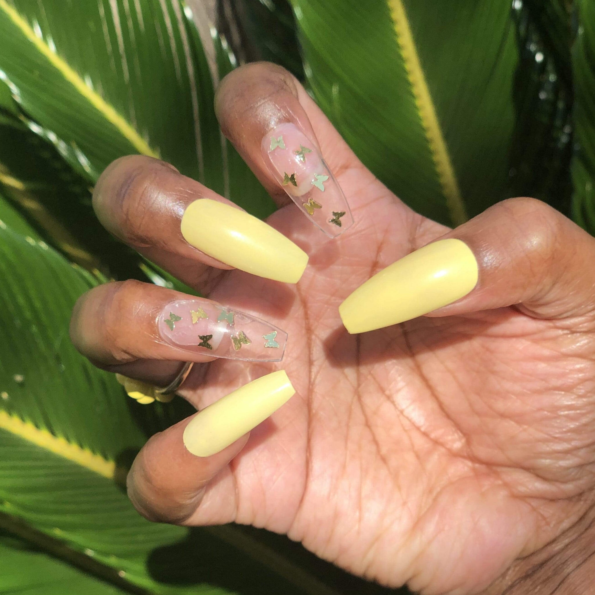 Manicure hand wearing light yellow nails. The index and ring finger nails are clear with yellow butterflies on them.