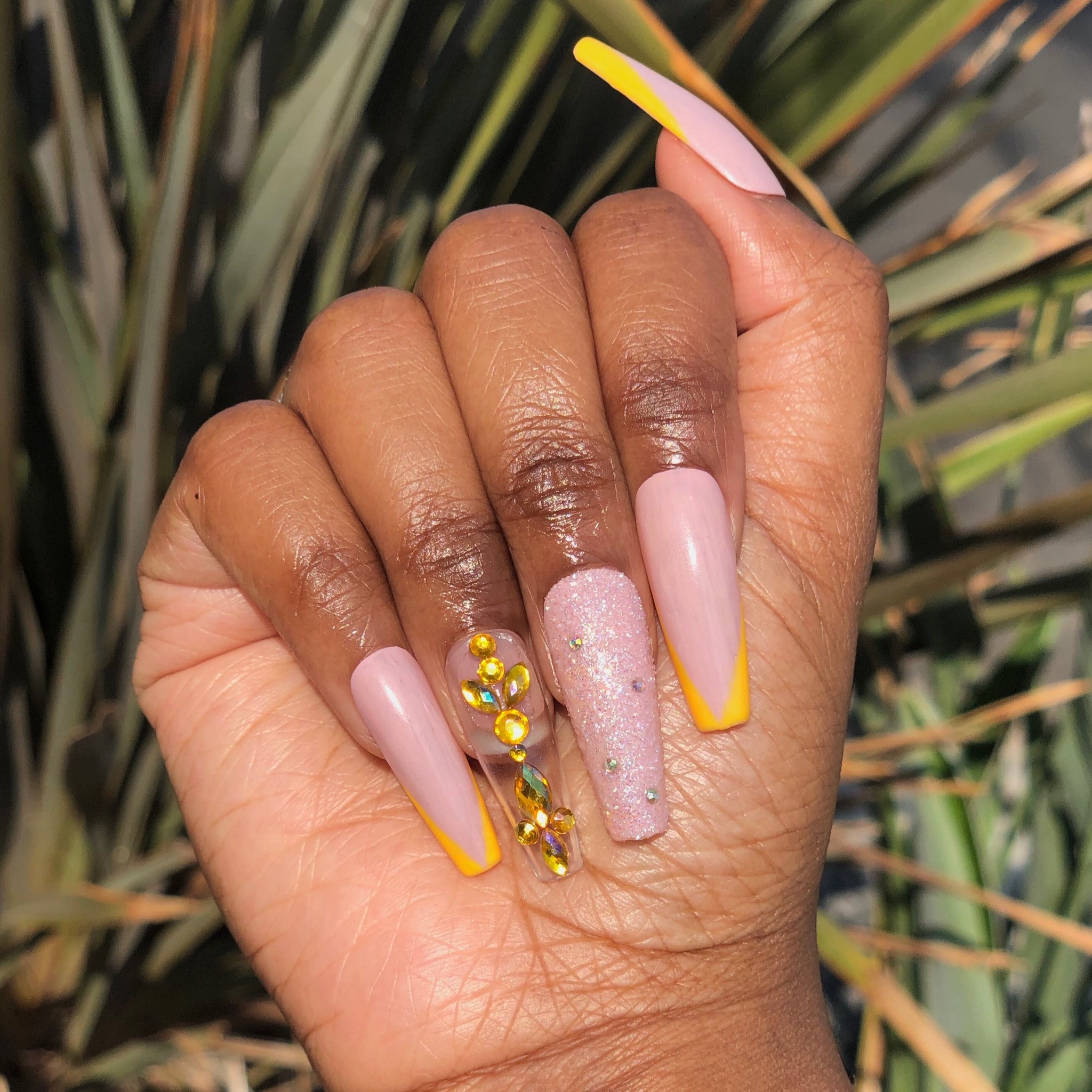 Manicure hand wearing tan press on nails with yellow French tip and multicolor yellow base  gems