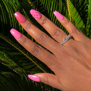 Manicure hand wearing pink nails with pink glitter on middle finger and pink rhinestones on ring finger.