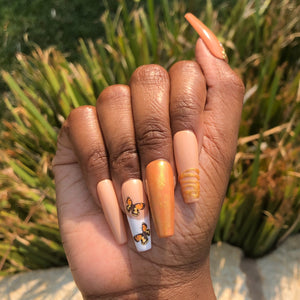 Manicure hand wearing orange press on nails with gold gems and French tip butterflies.